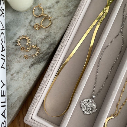 a gold snake chain necklace in a jewellery box compartment next to a silver durga coin charm on silver belcher chain